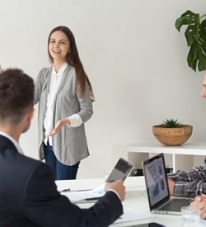 Smiling young employee or manager giving presentation working on flipchart in meeting room making business offer or reporting about project results, explaining new plan or idea to multi-ethnic team